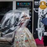 Una fallera se cubre con un plástico de camino a la ofrenda floral a la Virgen de los Desamparados