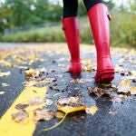 Mujer con botas de agua en una carretera pisando hojas