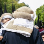 Un costalero de la Hermandad de la Sed de Sevilla lleva en brazos a su hijo, vestido con la misma indumentaria
