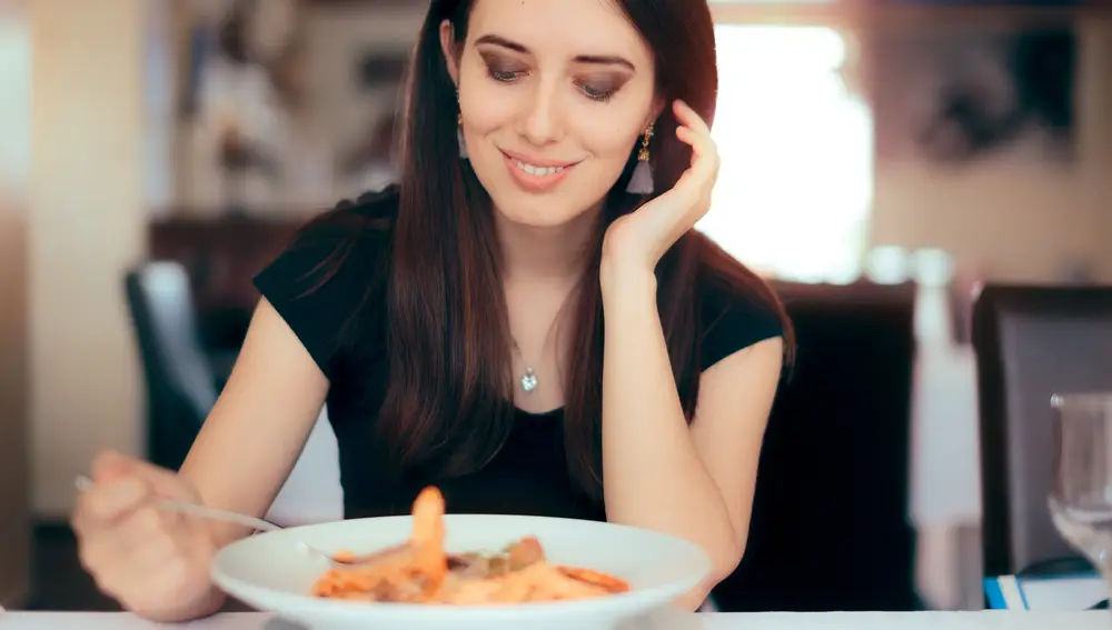 Mujer comiendo pasta con los codos en la mesa | Fuente: Dreamstime