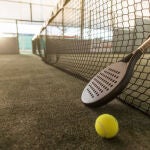 Paddle tennis image of outdoors court, racket, net and ball