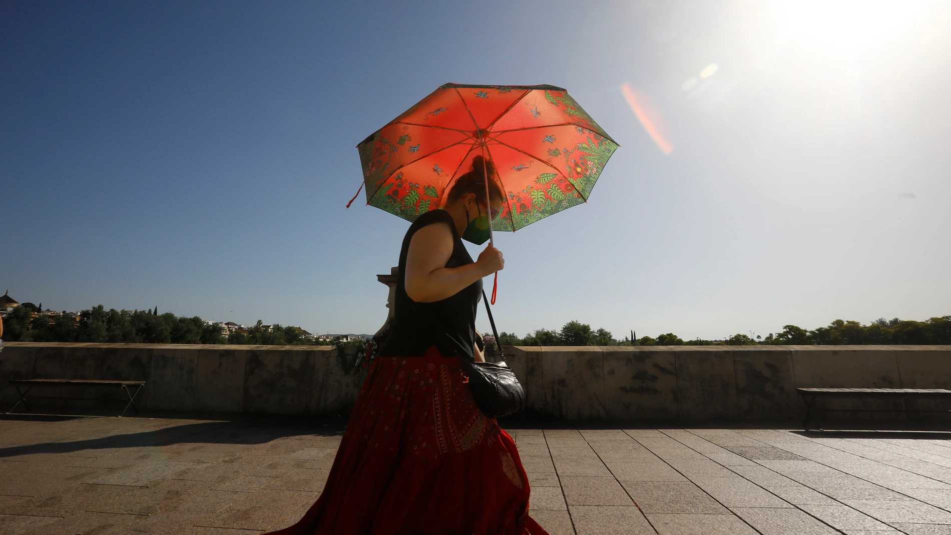 Una mujer se protege con un paraguas de las altas temperaturas mientras pasea por el puente Romano de Córdoba. EFE/Salas