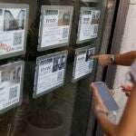 Unas personas se paran delante del escaparate de una inmobiliaria que publicita los inmuebles que gestiona, en el centro de Madrid