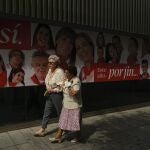 Personas paseando por Pamplona ante un cartel que anuncia los San Fermines, que comienzan el jueves, después de dos años sin celebrarse por la pandemia de covid