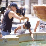 Una madre le echa agua a su hijo, por la cabeza, en la fuente de la plaza Virgen de los Reyes en Sevilla
