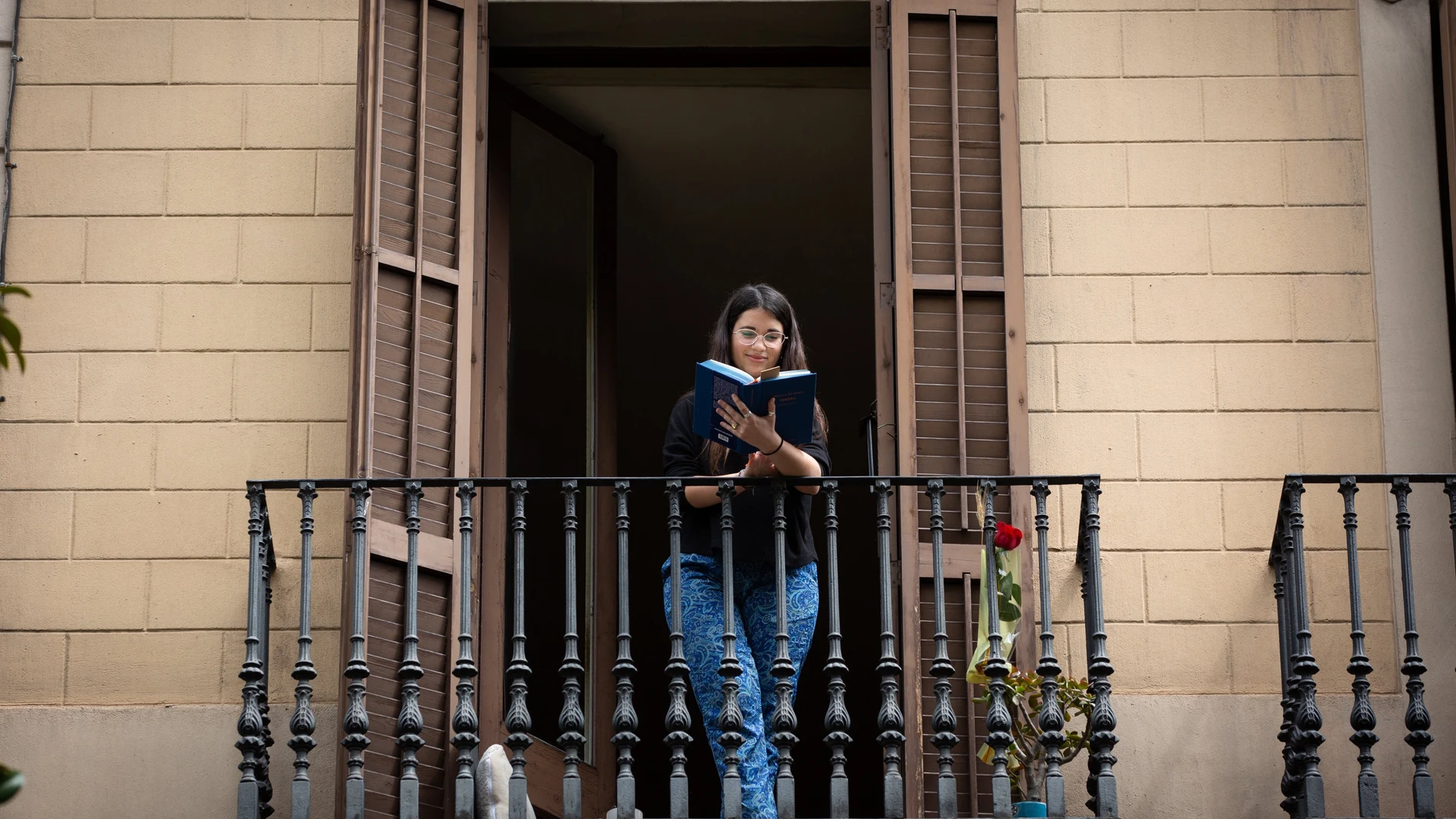 Una joven lee un libro en el balcón de su casa