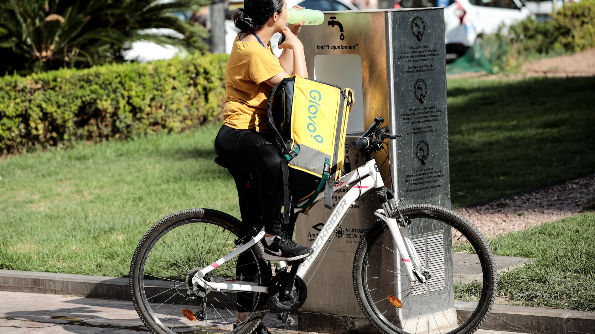 Una repartidora de comida a domicilio bebe agua de una fuente este viernes en la plaza del Ayuntamiento de València