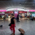 Viajeros pasan por delante de la oficina de Renfe, en la estación de Atocha