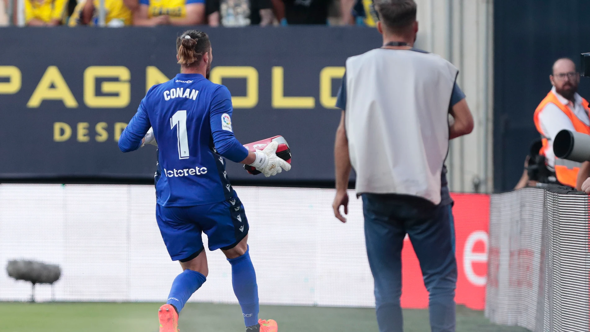 El portero del Cádiz CF, Ledesma, corre hacia la grada con un desfibrilador tras sufrir un aficionado un infarto durante el partido de LaLiga que enfrenta al Cádiz CF y al Barcelona CF en el estadio Nuevo Mirandilla de Cádiz este sábado. EFE/Román Ríos.