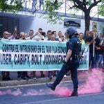 Un policía nacional retira de una patada un bote de humo durante la nueva concentración de taxistas frente a la Consejería de Fomento contra la regulación que prepara la Junta para los VTC