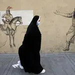 Una mujer iraní con velo pasa junto a una pared dibujada en Teherán