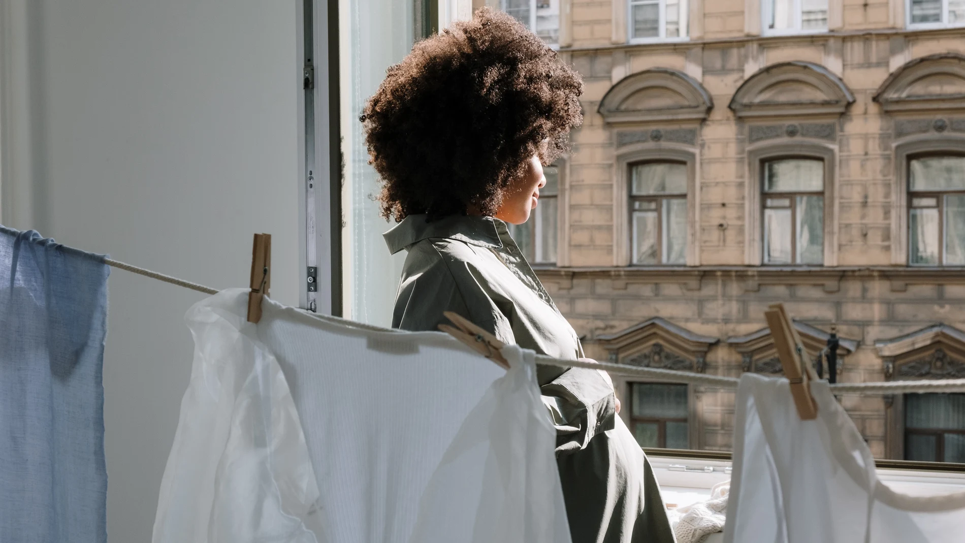 Mujer mirando por la ventana junto a ropa tendida