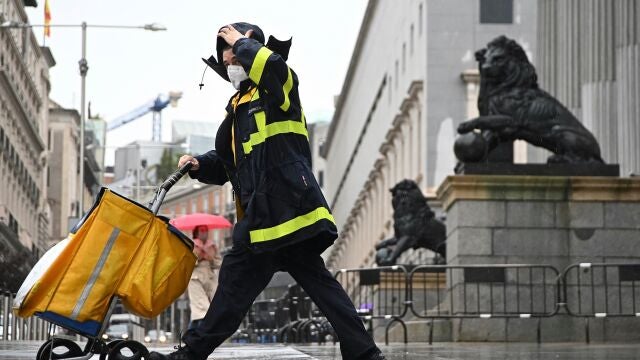 Un trabajador de Correos, bajo la lluvia, a su paso por el Congreso de los Diputados de Madrid