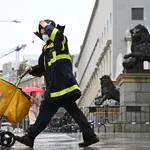 Un trabajador de Correos, bajo la lluvia, a su paso por el Congreso de los Diputados de Madrid