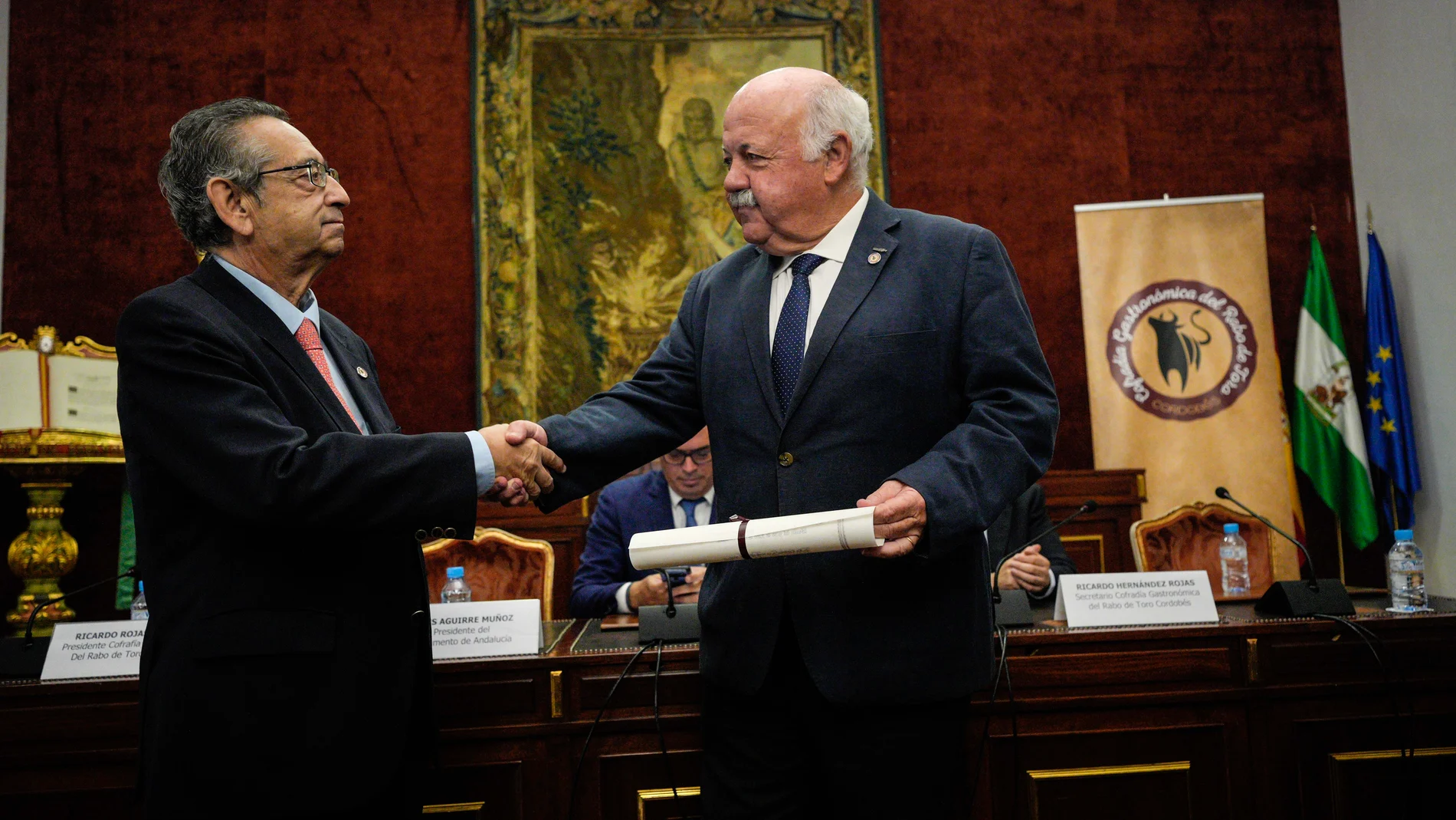 El presidente de la Cofradía Gastronómica del Rabo de Toro Cordobés, Ricardo Rojas (i), hace entrega al presidente del Parlamento de Andalucía, Jesús Aguirre, de la insignia y el diploma como cofrade de honor de esta hermandad