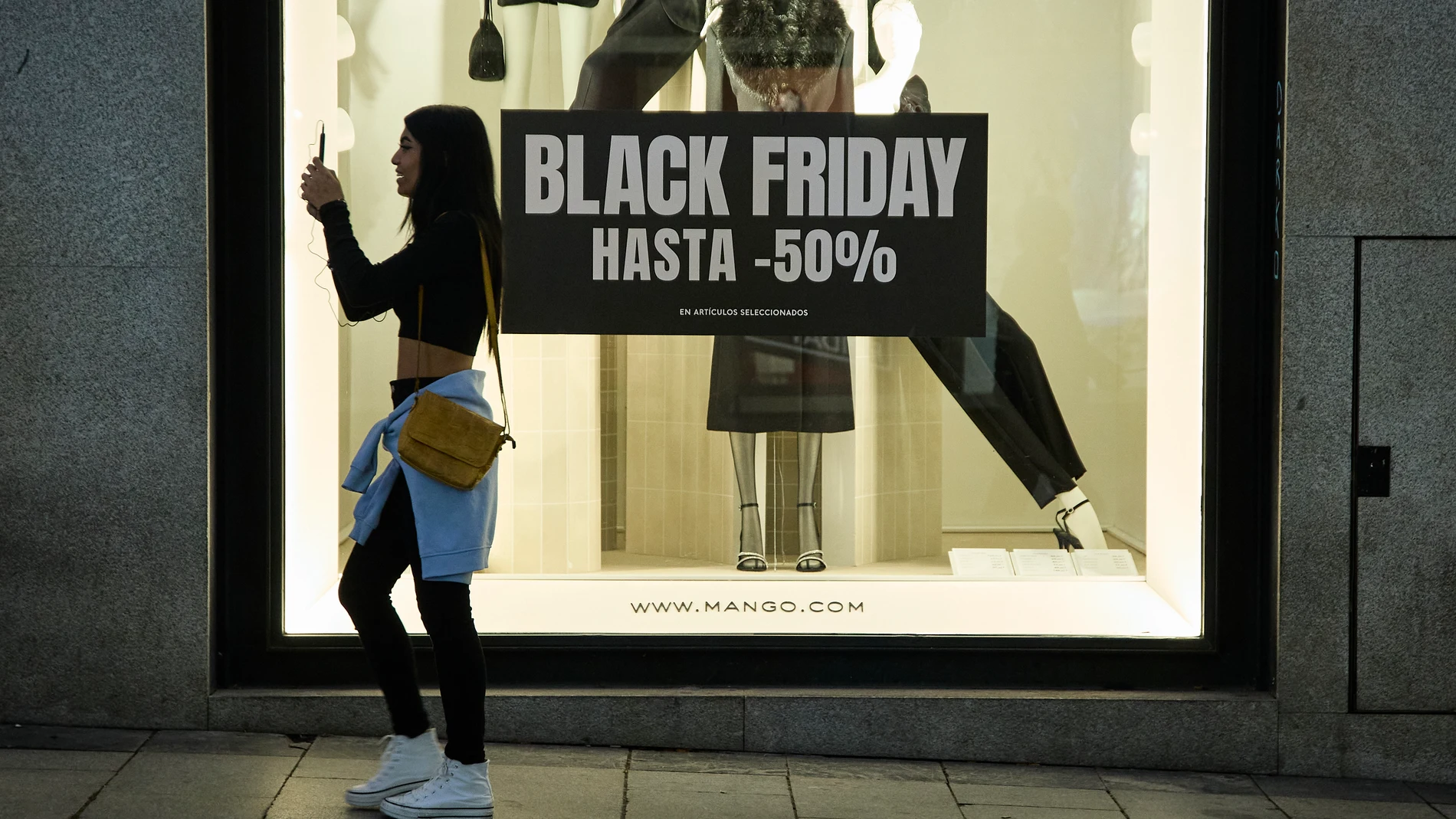 Varias personas pasan por delante de los comercios que anuncian los descuentos del "Black Friday", a 23 de noviembre de 2022, en Madrid