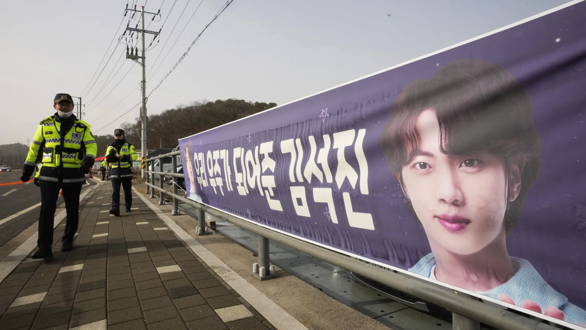 Policías surcoreanos pasan junto a un poster con la cara de Jin, el primer miembro de BTS que ingresa en el servicio militar