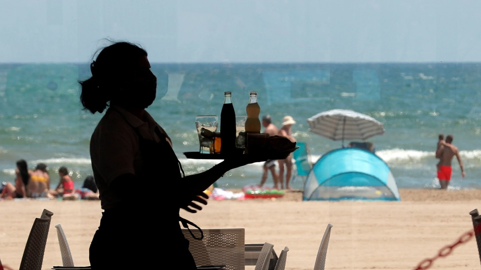Una camarera lleva una bandeja en la playa valenciana de la Malvarrosa