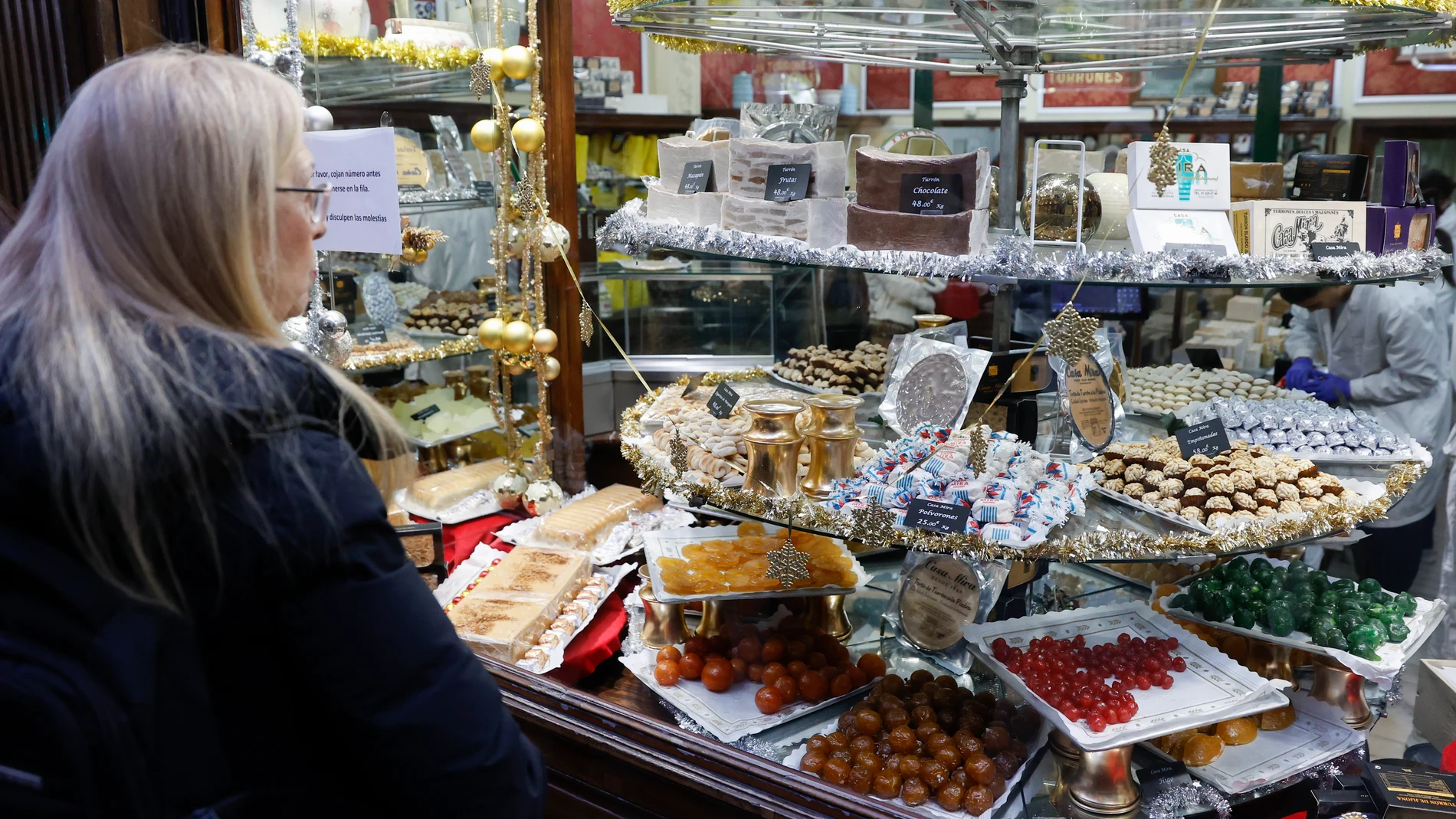 GRAF9162. MADRID 22/12/2022.- Viandantes y clientes observan los escaparates de la capital madrileña este jueves, donde se muestran dulces típicos de Navidad. El fuerte alza del precio de las materias primas ha supuesto que este año los turrones cuesten un 10% más que hace un año, pero a pesar de ello no faltarán en la cena de esta Nochebuena. EFE/ Mariscal