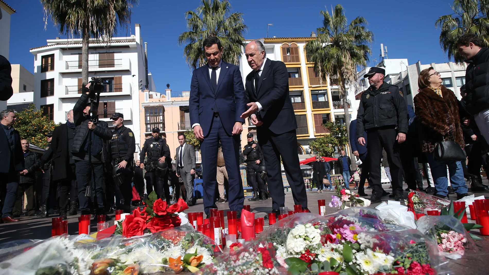 El presidente de la Junta de Andalucía, Juanma Moreno junto con el alcalde de Algeciras, José Ignacio Landaluce, ante las flores y velas dejadas en la plaza en la que fue asesinado el sacristán de la Iglesia de La Palma, Diego Valencia