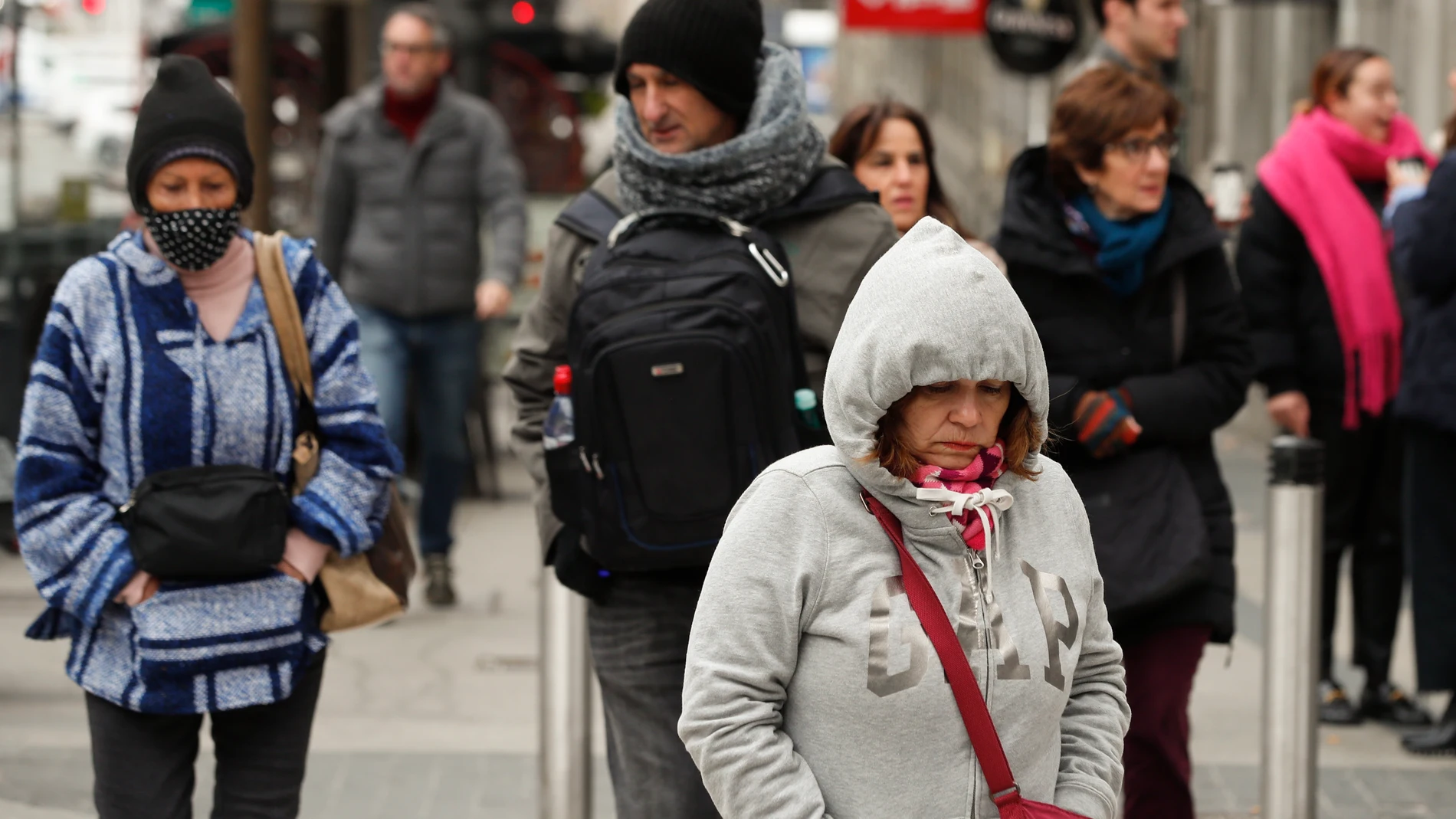 GRAF9585. MADRID, 07/02/2023.- Varias personas caminan por una calle de Madrid, abrigados con gorros y bufandas para intentar mitigar las bajas temperaturas registradas este martes. Once comunidades están en alerta meteorológica por nevadas, lluvias, viento, frío, oleaje y tormentas, de las cuales Andalucía, Baleares, Cataluña y Comunidad Valenciana están en color naranja por riesgo importante, especialmente la franja mediterránea, con olas de hasta 9 metros y rachas intensas. EFE/ Eduardo Oy...