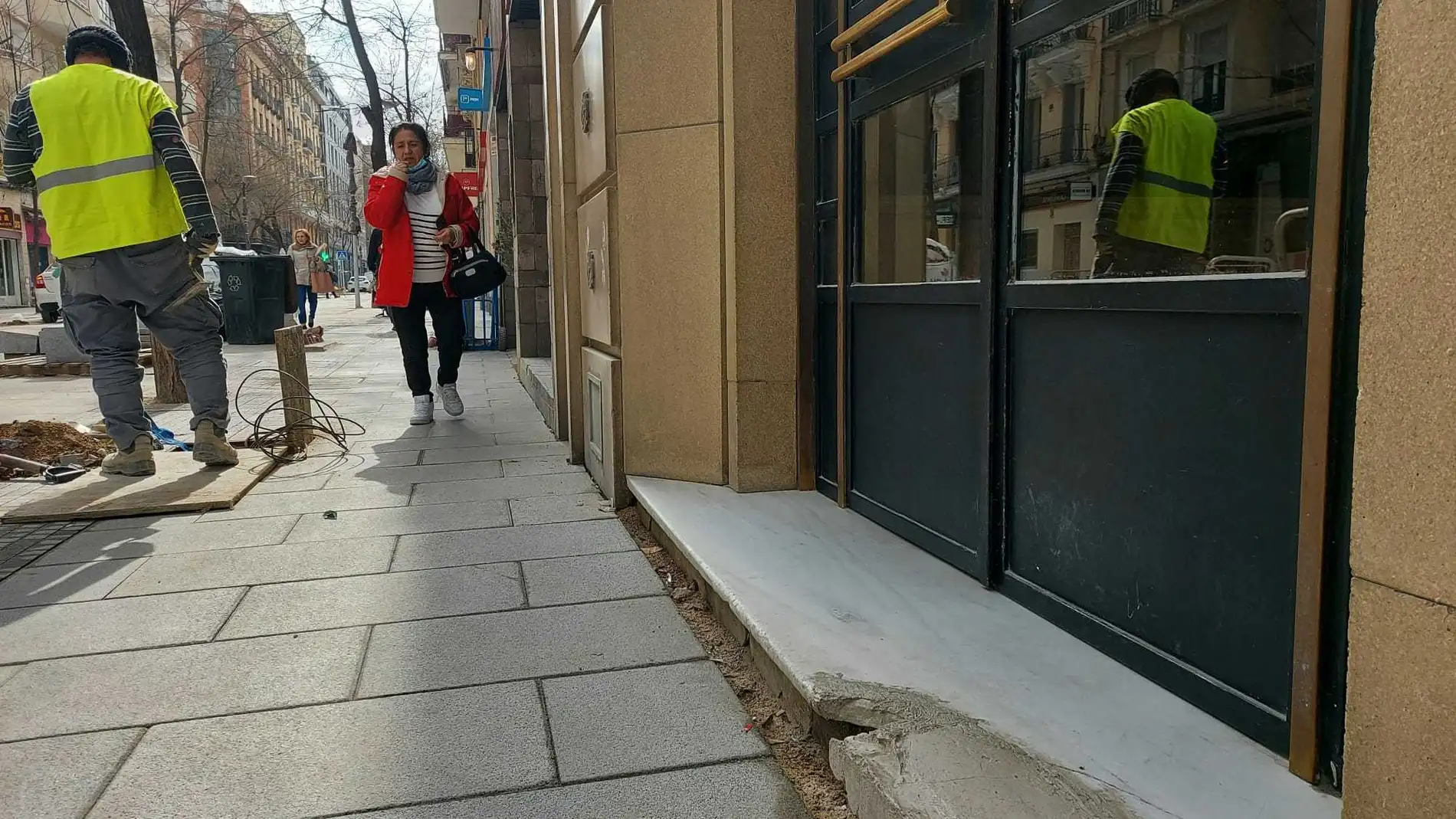 Una mujer camina junto a un hoyo lleno de cables no señalizado en el portal de la calle Ponzano número 59, dañado por las obras de ampliación de las aceras