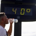 Un joven bebe agua junto a un termómetro de calle que marca 40 grados
