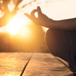 Mujer practicando yoga y meditación en posición de loto en la puesta de sol.