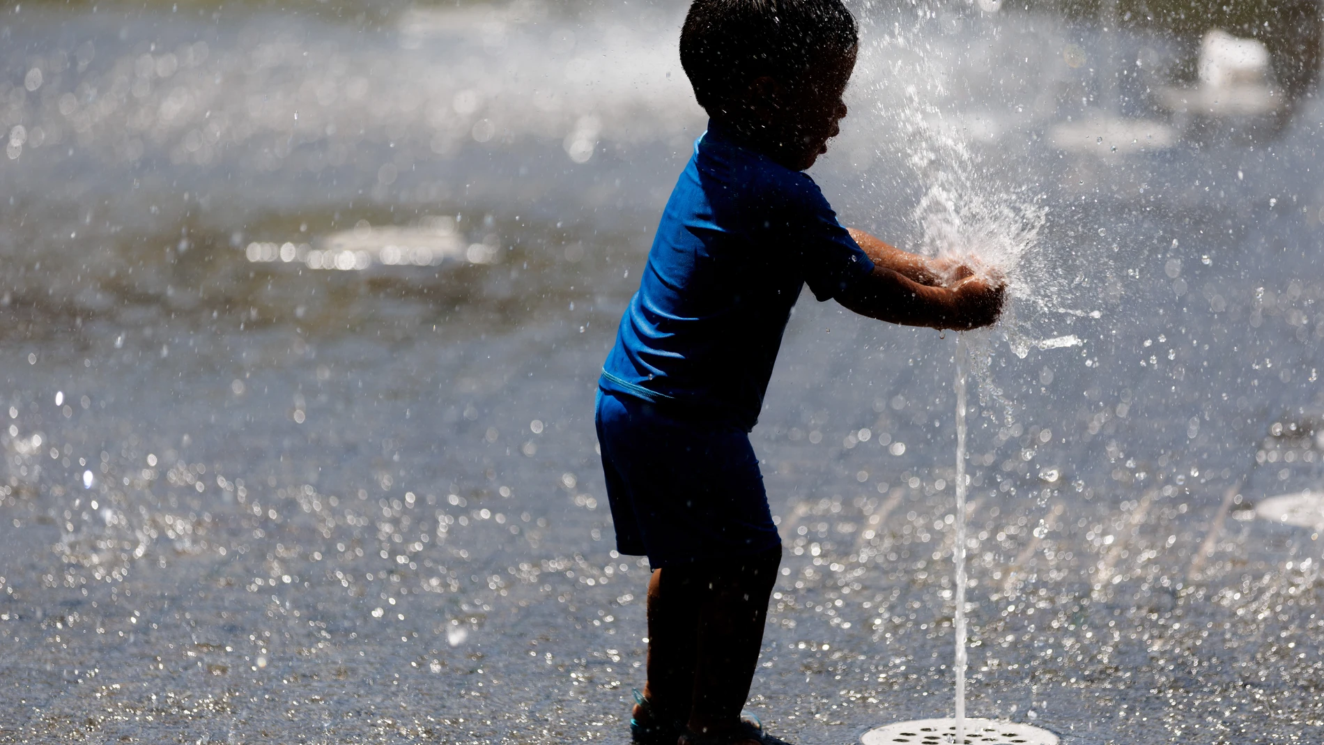 Un niño juega con el agua en una fuente de Madrid
