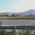 Un ciclista pedalea en la carretera con la granja que sale a subasta por un euro al fondo