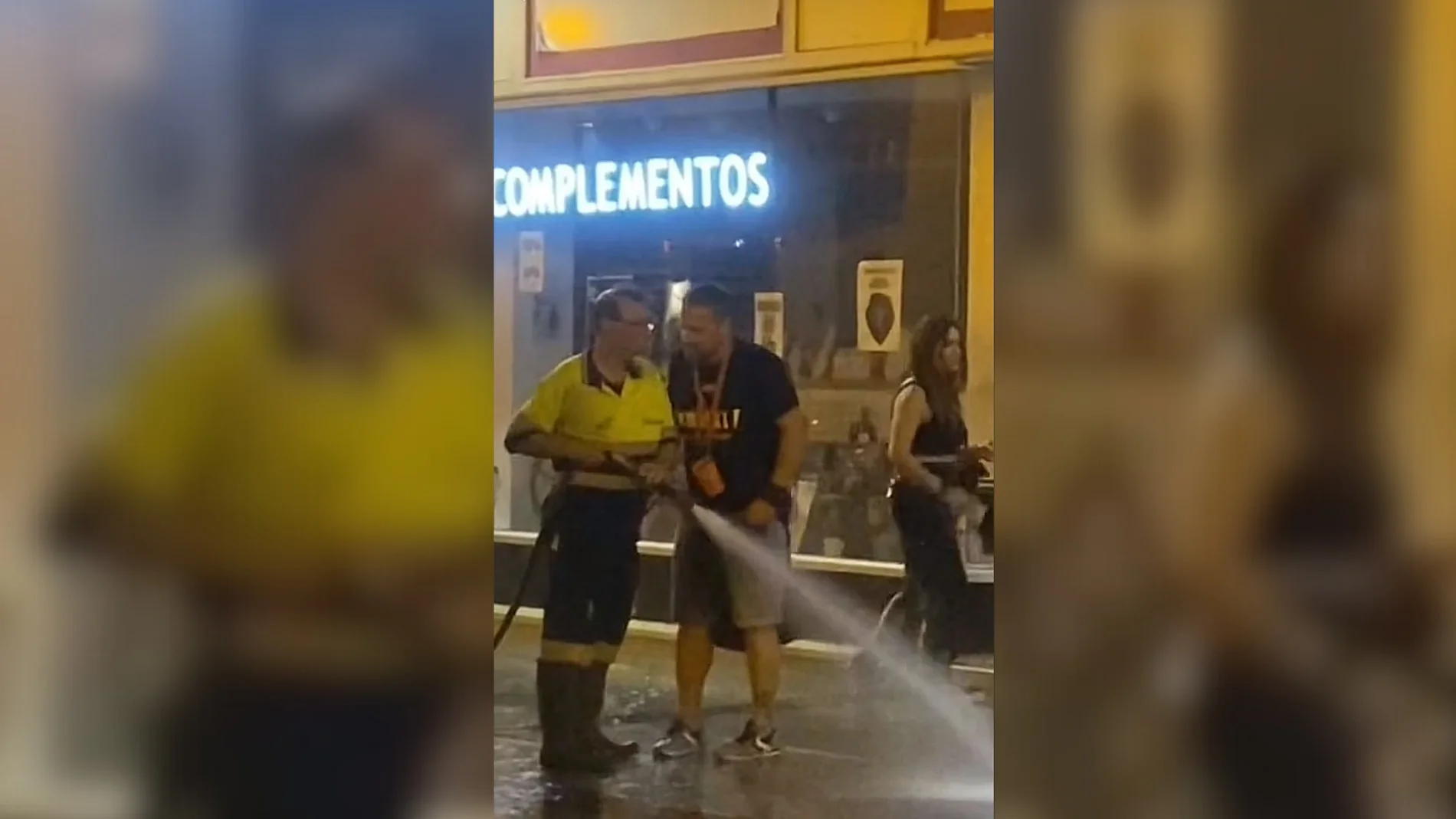 Un trabajador de la limpieza da un manguerazo a una mujer para que se aparte