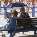 Imagen de dos mujeres protegiéndose del sol y del calor con abanico y parasol.