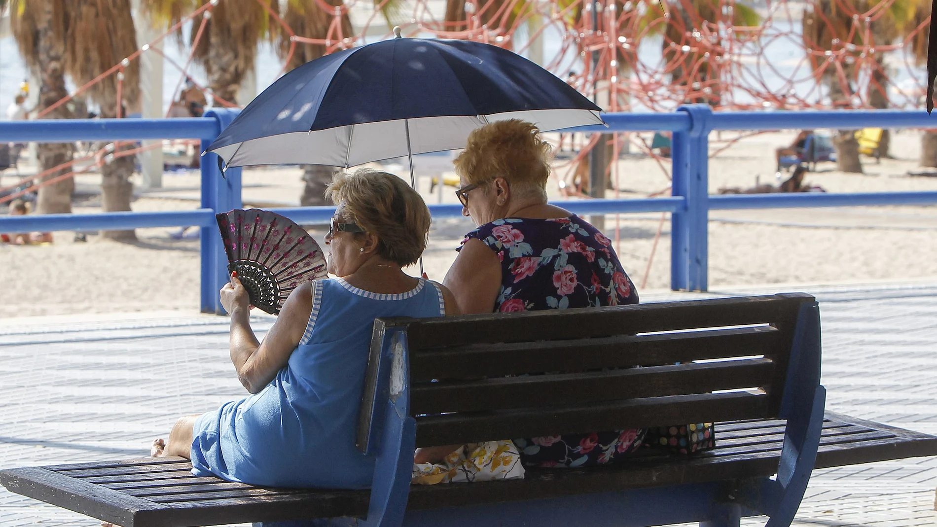 Imagen de dos mujeres protegiéndose del sol y del calor con abanico y parasol.