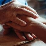 Manos de persona mayor y persona joven entrelazadas