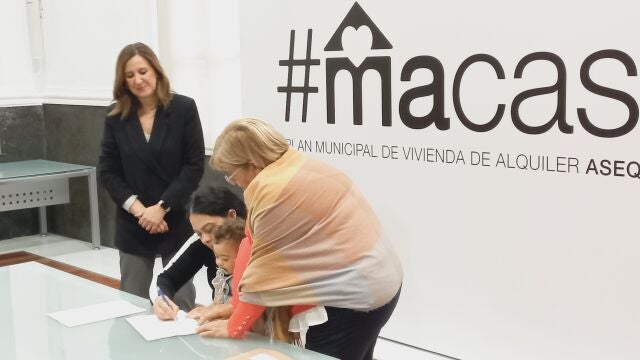 Una madre con su bebé en brazos firma el contrato de alquiler en presencia de la alcaldesa