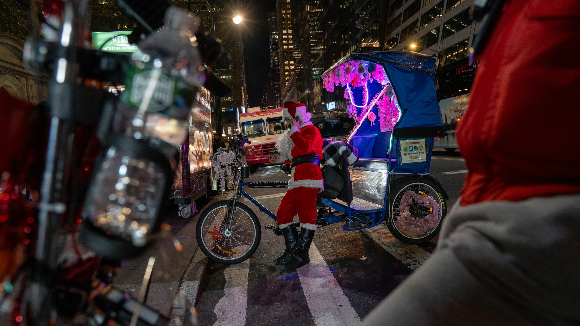 ACOMPAÑA CRÓNICA: EEUU NAVIDAD - AME5017. NUEVA YORK (ESTADOS UNIDOS), 18/12/2023.- Una persona disfrazada de Papá Noel espera clientes para su bicitaxi frente a la plaza de Bryant Park, el15 diciembre de 2023, en Nueva York (EE.UU.). La Navidad en Nueva York, como en el resto de las grandes metrópolis del mundo, ha perdido casi por completo su original sentido religioso y se reduce a poco más que un pino decorado con figuritas intrascendentes y luces, así como coronas vegetales, aunque en es...