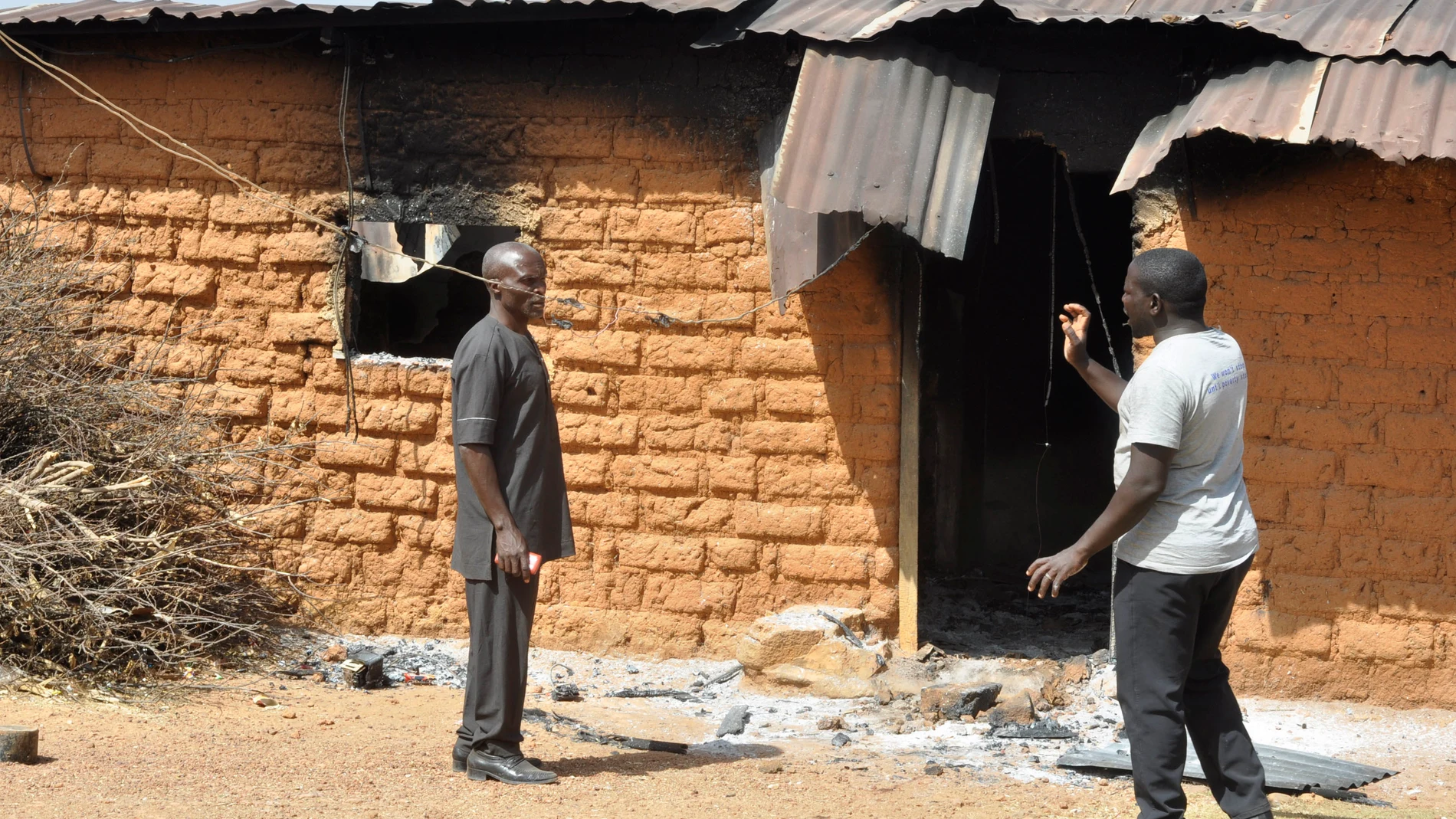 People stand in front of a burnt house following an attacked by gunmen in Bokkos, north central Nigeria, Tuesday, Dec. 26, 2023. Nigerian officials and survivors say at least 140 people were killed by gunmen who attacked remote villages in north-central Nigeria's Plateau state in the latest of such mass killings this year blamed on the West African nation's farmer-herder crisis. (AP Photo)