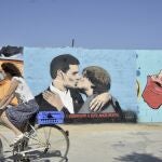 Un ciclista pasa al lado del mural del presidente español y candidato del PSOE a la reelección Pedro Sánchez y al expresidente de la Generalitat y eurodiputado de Junts, Carles Puigdemont, dándose un beso en el mural del artista urbano TVBoy, en la plaza de las Glòries, en Barcelona, 