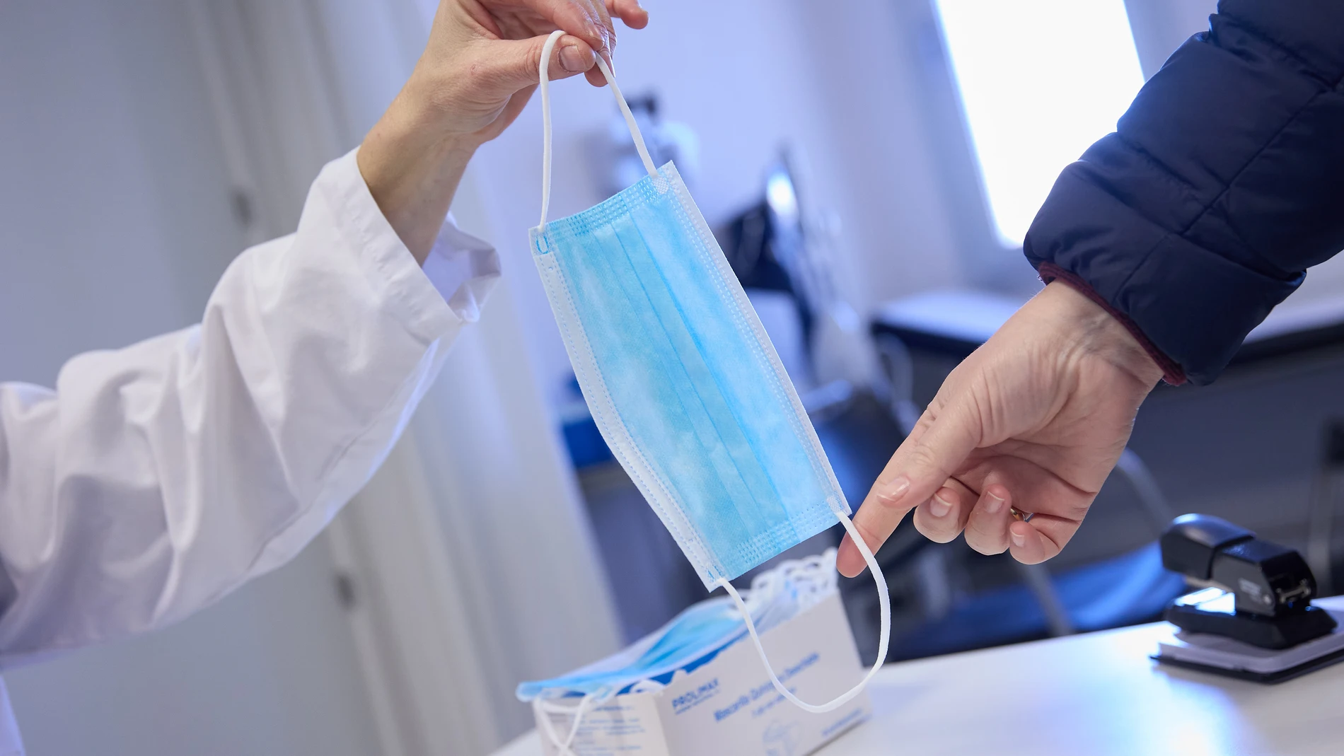 Una sanitaria ofrece una mascarilla a un paciente en el centro de salud 'Isla de Oza', a 11 de enero de 2024, en Madrid (España). El ministerio de Sanidad ha implantado desde ayer, 10 de enero, el uso obligatorio de mascarillas en hospitales y centros sanitarios, una vez que se comunique a las comunidades autónomas. El uso obligatorio de la mascarilla es una orden notificada que no tiene que publicarse en el Boletín Oficial del Estado (BOE). Sanidad ha tomado esta decisión después de no haber...