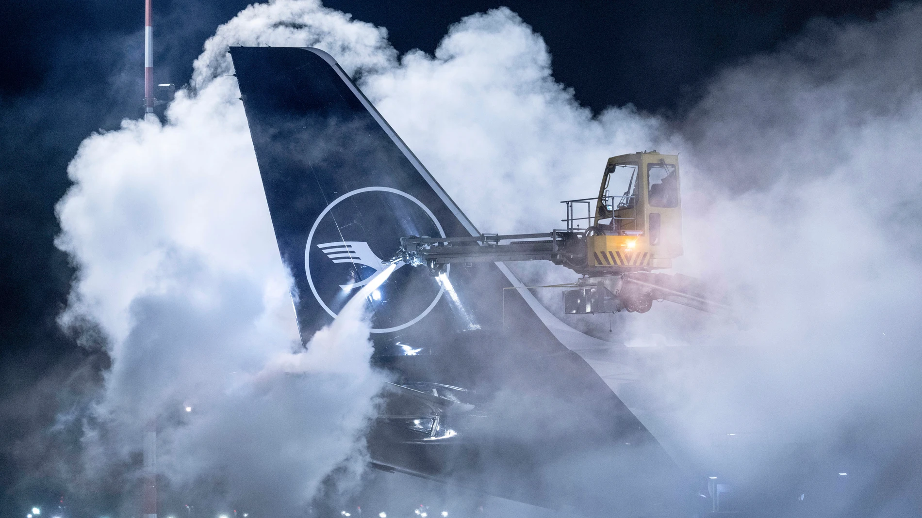 A Lufthansa aircraft is de-iced at Frankfurt Airport, Germany, early Wednesday, Jan. 17, 2024. Heavy snowfalls and freezing rain across Germany Wednesday led to the cancellation of hundreds of flights and trains, crashes on icy roads, and school closures. (Boris Roessler/dpa via AP)