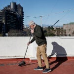 Un vecino de Campanar limpia su terrraza de cenizas. Al fondo, los dos edificios arrasados por el fuego 