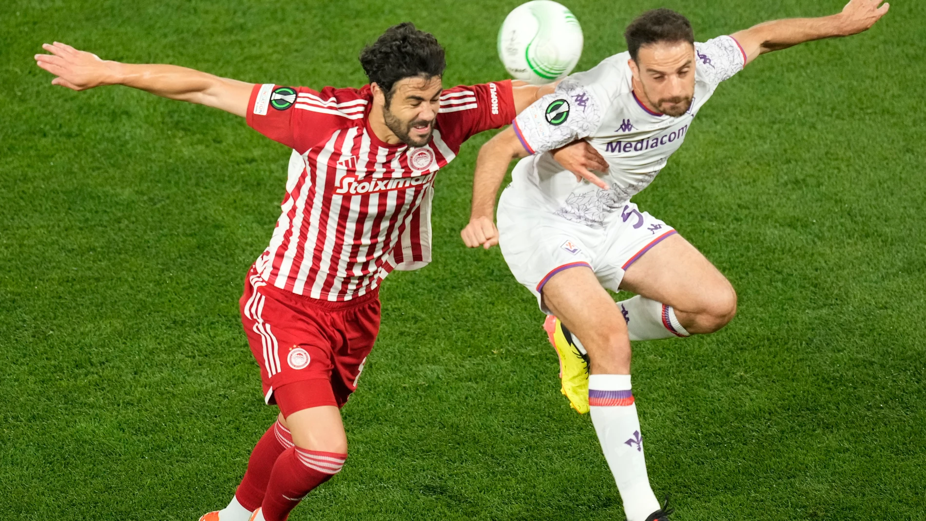 Olympiacos' Vicente Iborra, left, jumps for a header with Fiorentina's Giacomo Bonaventura during the Conference League final soccer match between Olympiacos FC and ACF Fiorentina at OPAP Arena in Athens, Greece, Wednesday, May 29, 2024. (AP Photo/Petros Karadjias)