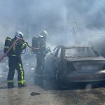 Los bomberos intentan sofocar las llamas de uno de los vehículos calcinados