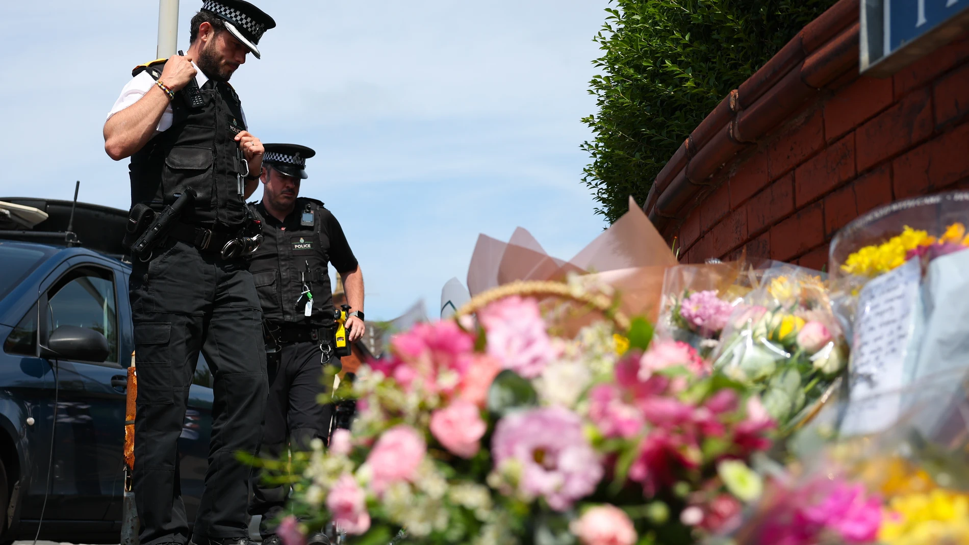 Southport (United Kingdom), 30/07/2024.- Police officers look at tributes left at the scene of a stabbing attack at the junction with Hart Street in Southport, Britain, 30 July 2024. Merseyside Police confirmed on 30 July that a third child aged 9 has died as a result of a knife attack in Southport the previous day, and confirmed that the other two victims were ages six and seven respectively. Five other children and two adults remain in critical condition. Armed police detained a 17-year-old...