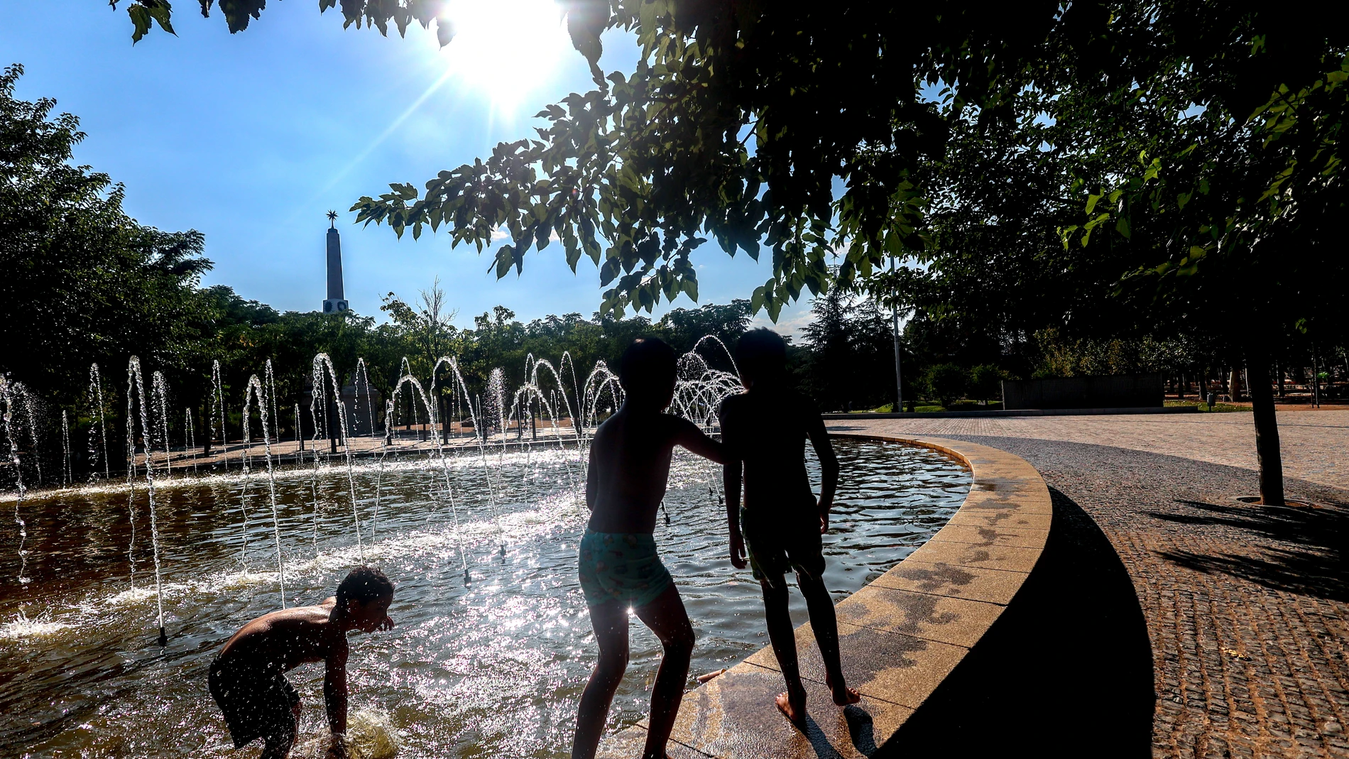 Tres niños se refrescan en una fuente durante la tercera ola de calor en Madrid, en el parque Madrid Río, a 3 de agosto de 2024, en Madrid (España). La Comunidad de Madrid mantiene activado el nivel dos de Alto Riesgo por altas temperaturas ante la previsión de temperaturas máximas por encima de 38,5 grados para el próximo lunes 5 de agosto, tras el descenso de las temperaturas máximas que se está registrando este fin de semana. 03 AGOSTO 2024;CALOR;OLA DE CALOR;AGUA;FUENTES;MADRID RÍO;TEMPE...