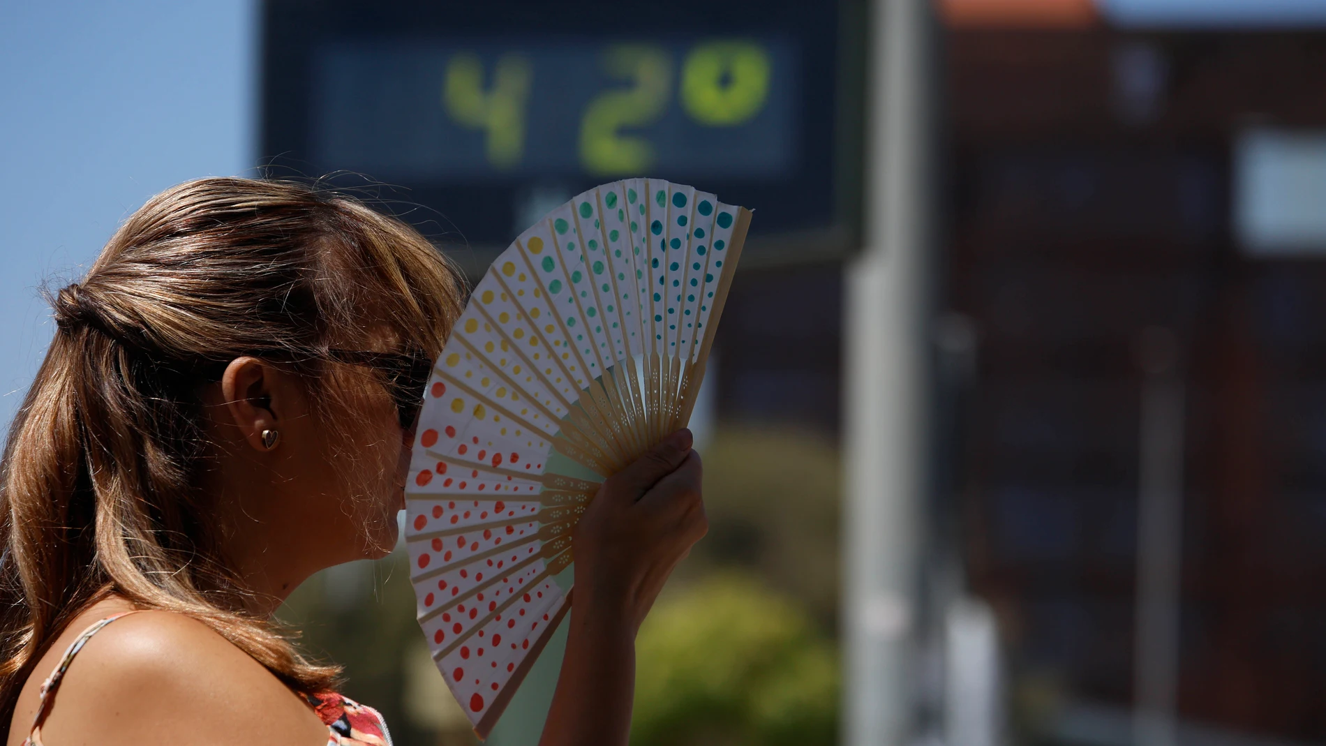 Una mujer se abanica junto a un termómetro de calle que marca 42 grados