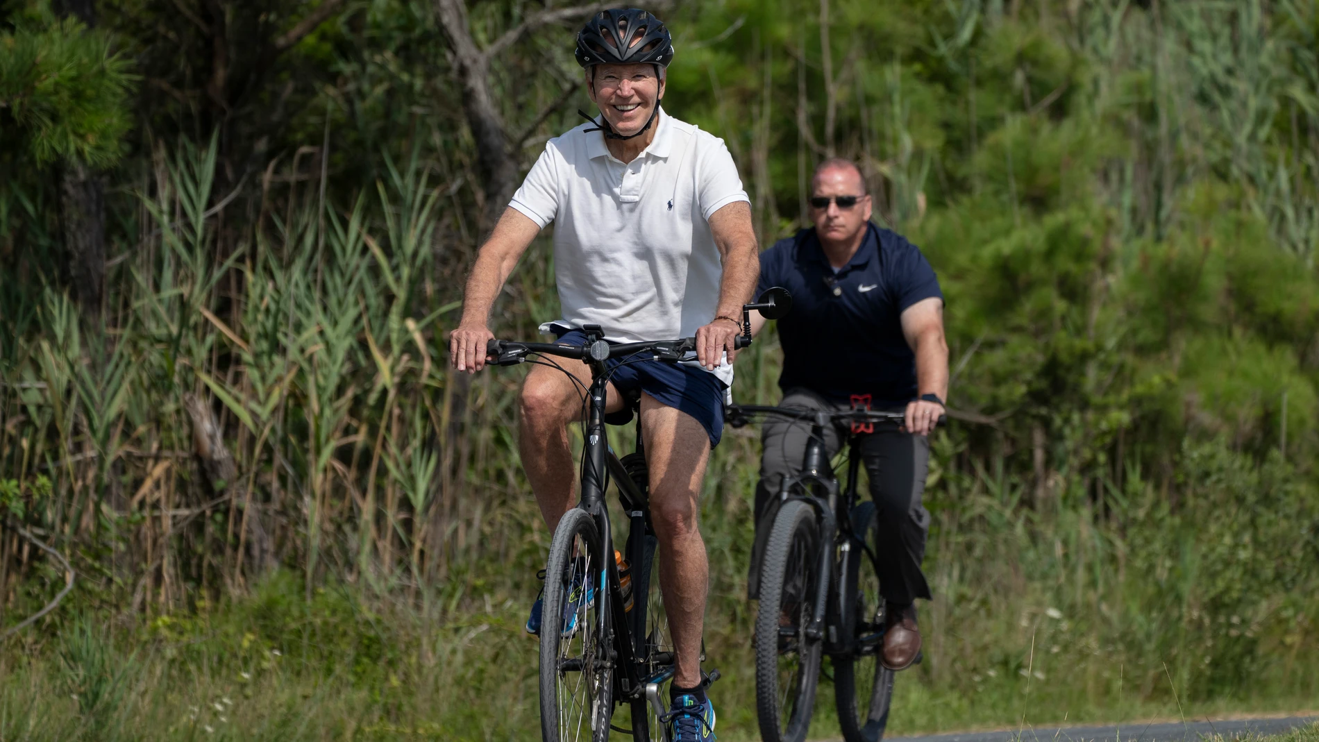 Joe Biden sonríe mientras monta en bicicleta flanqueado por el servicio secreto