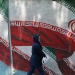 Una mujer pasa junto a un mural de la bandera de Irán en Teherán