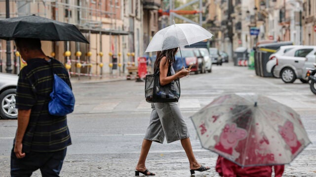 Varias personas caminan bajo la lluvia por una calle del centro de Valencia