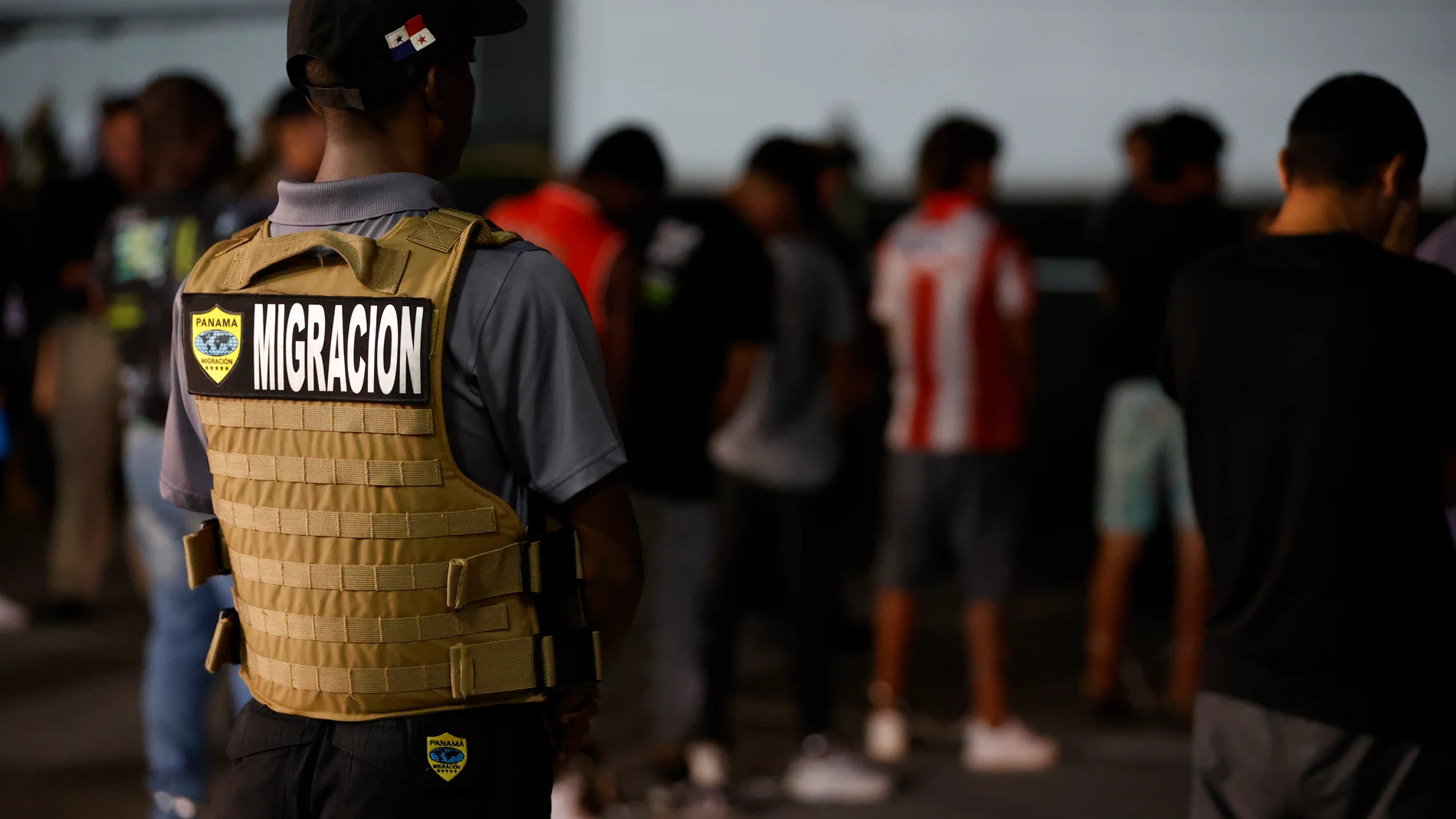 AME1955. CIUDAD DE PANAMÁ (PANAMÁ), 20/08/2024.- Un agente de migración de Panamá vigila a migrantes luego de ser deportados de los Estados Unidos este martes, en el aeropuerto Marcos A. Gelabert en Ciudad de Panamá (Panamá). Un primer grupo de migrantes, que cruzó el Darién ilegalmente, regresó al país centroamericano de acuerdo a un memorando de entendimiento entre los gobiernos de Panamá y los Estados Unidos. EFE/ Bienvenido Velasco